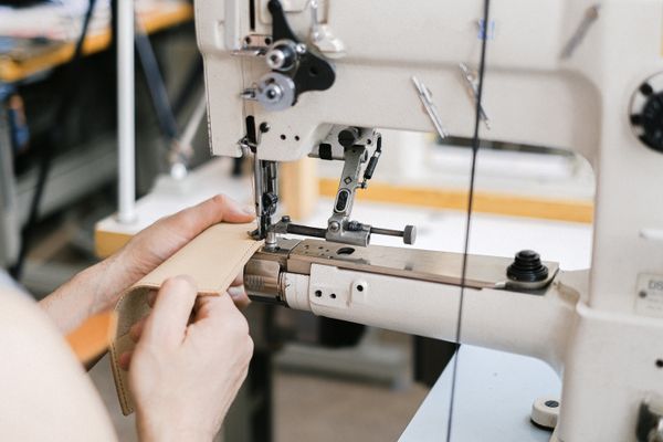 Hands guiding leather through an industrial sewing machine